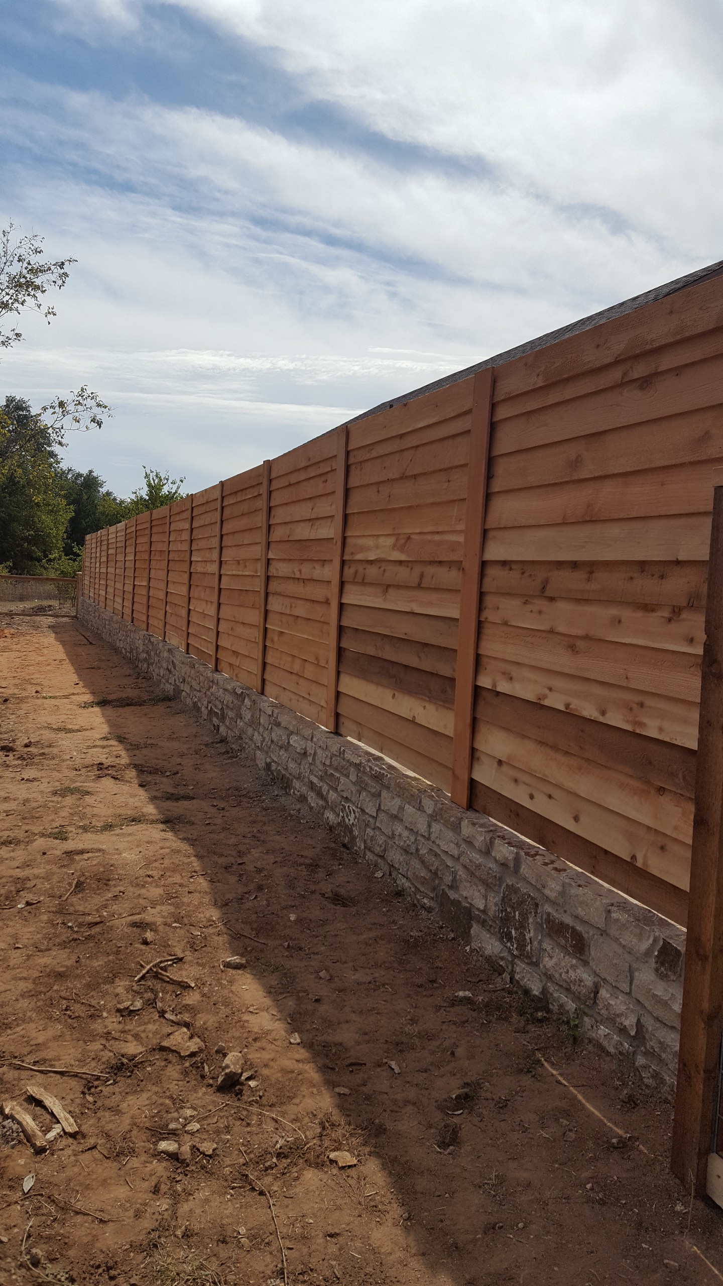 Long run of horizontal cedar plank privacy fence built on a stone foundation wall by All Around Fencing