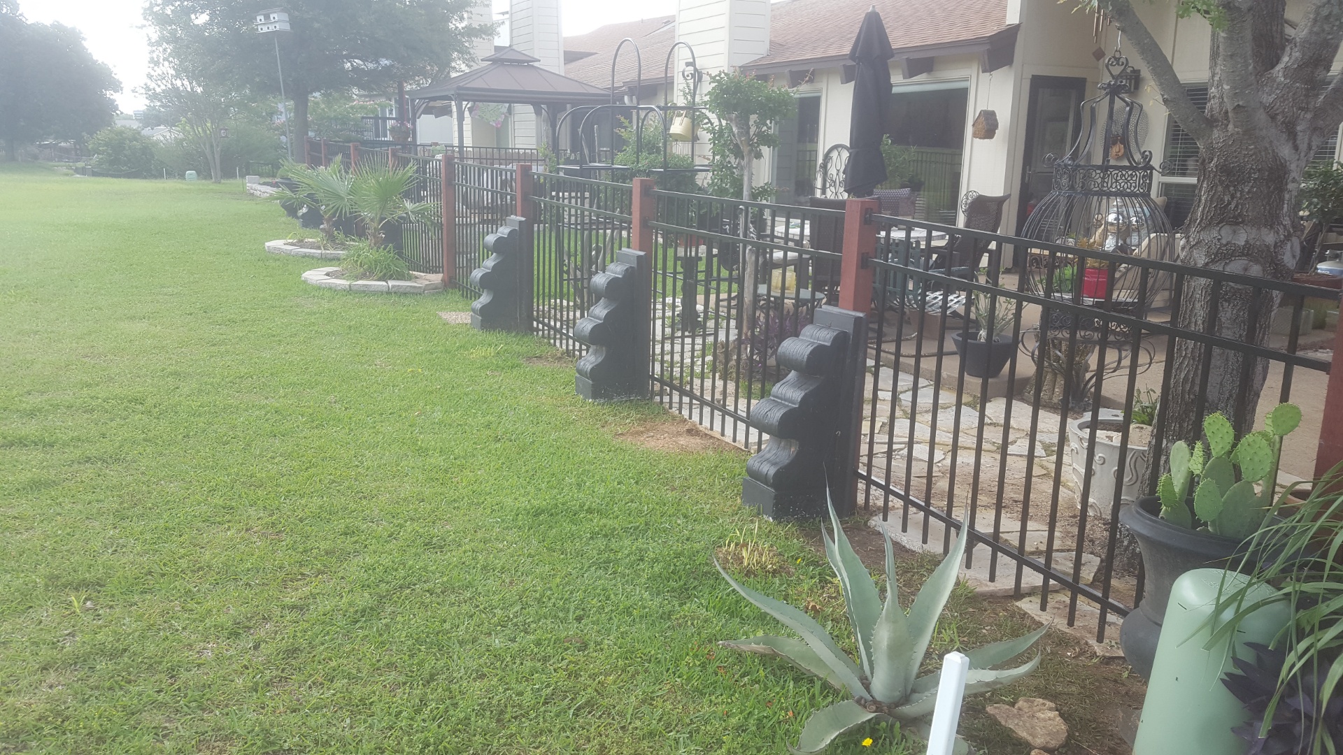 Black ornamental iron fence with decorative post caps enclosing a lakeside patio